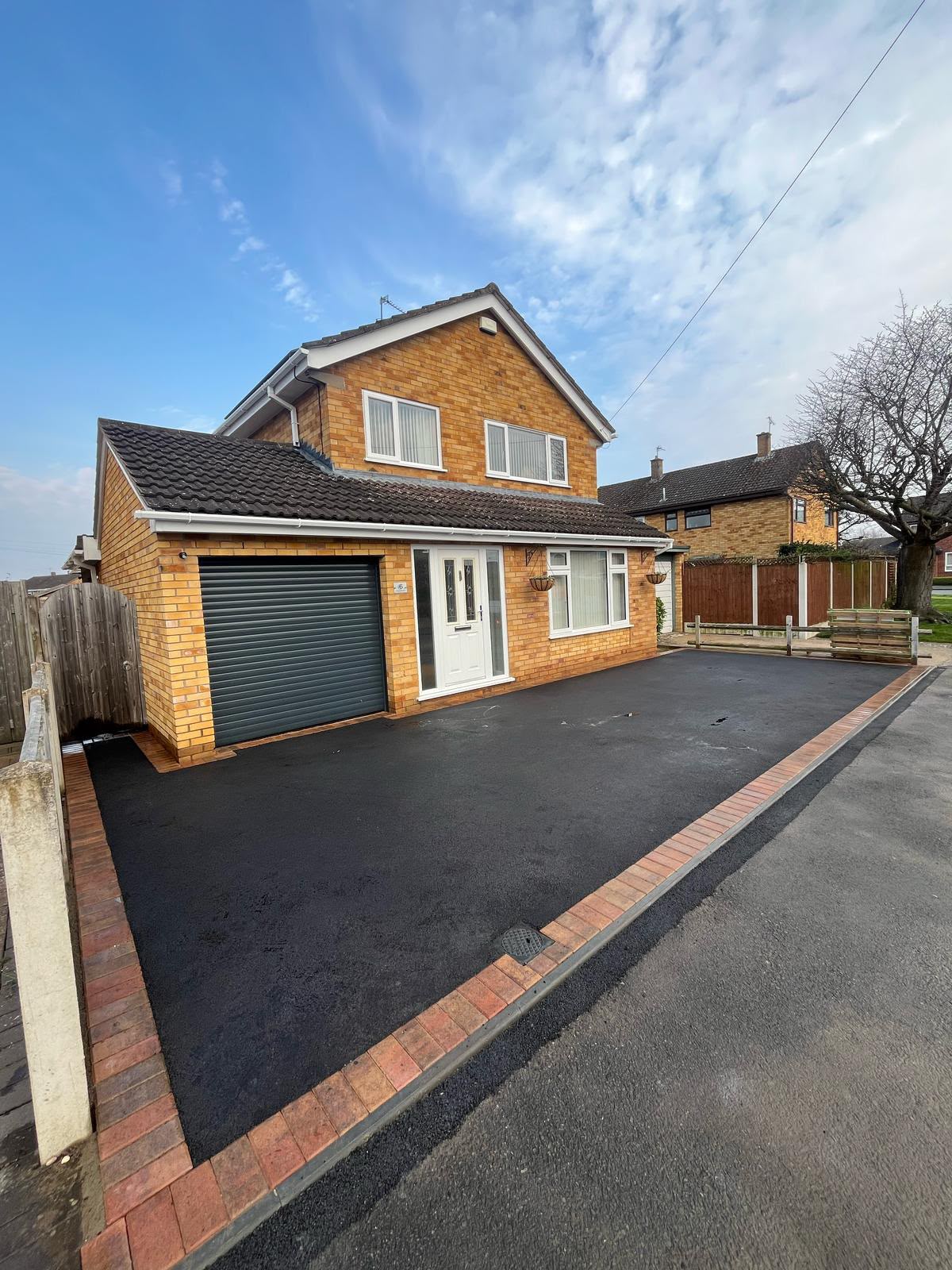 New tarmac driveway with red brick soldier course edging in front of a detached property